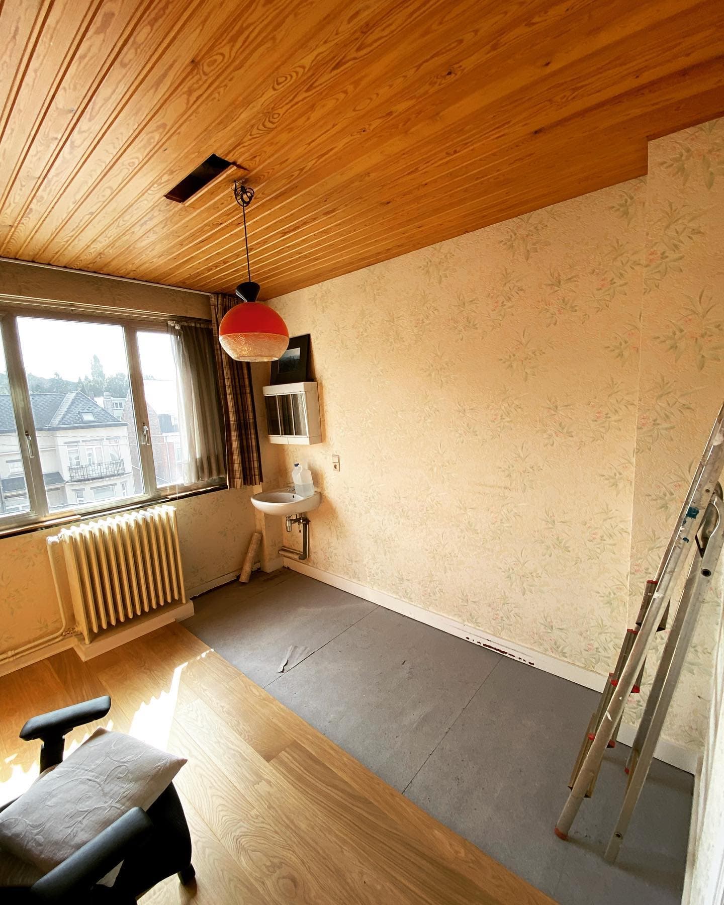 Kamer voor de renovatie: oud behang, een radiator en een wandlavabo
